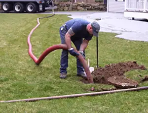 Septic pumping technician servicing a residential septic tank with a vacuum hose in Warwick, RI