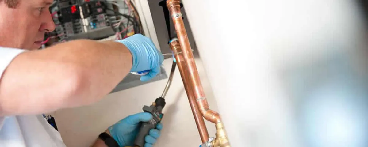 Water heater repair technician testing copper pipe connections and controls in Warwick, RI