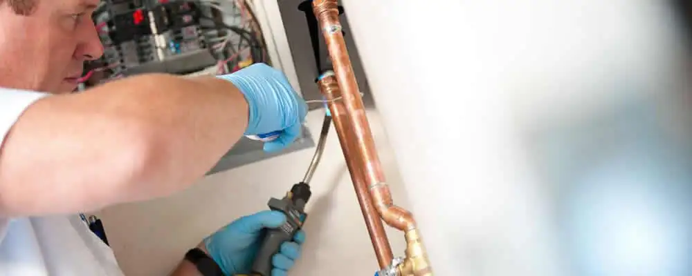 Water heater repair technician testing copper pipe connections and controls in Warwick, RI